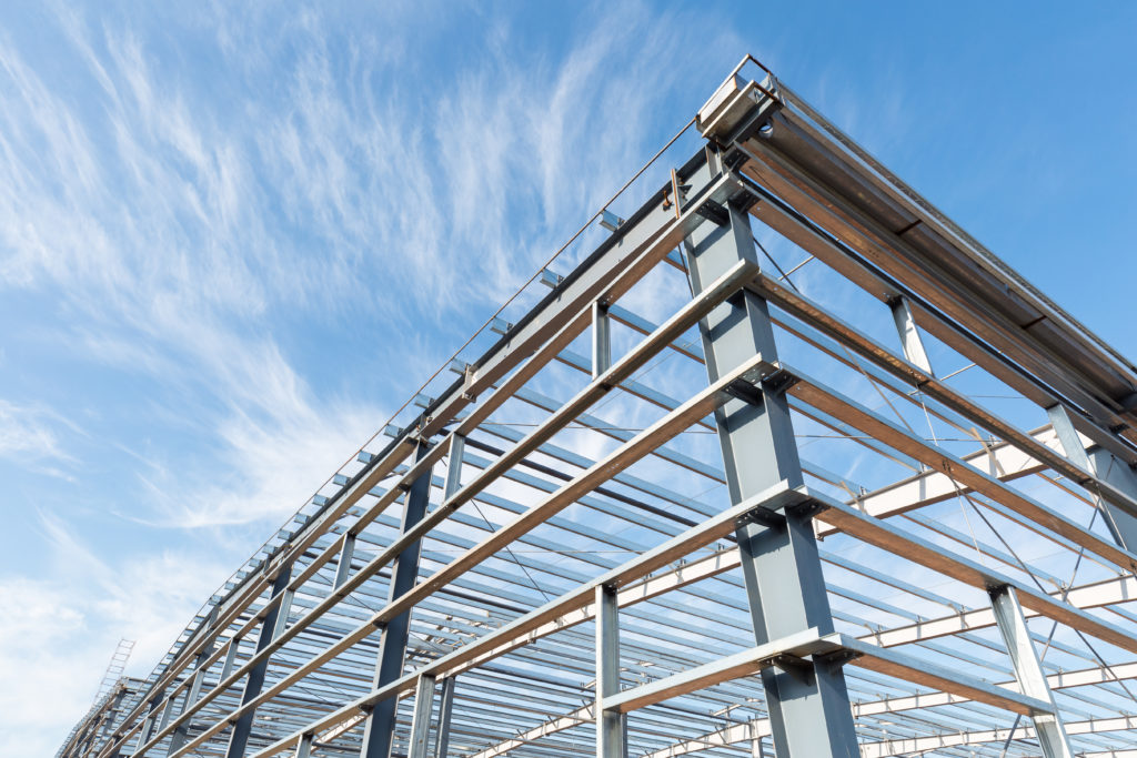 Steel frame workshop standing under construction below a blue, overcast sky.