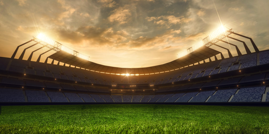 Empty baseball stadium with a clear and green field of grass with the sun setting in the horizon. 