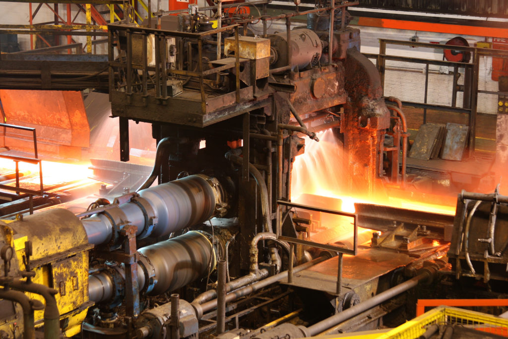 Hot steel being rolled to shape in mill in steel manufacturing plant.