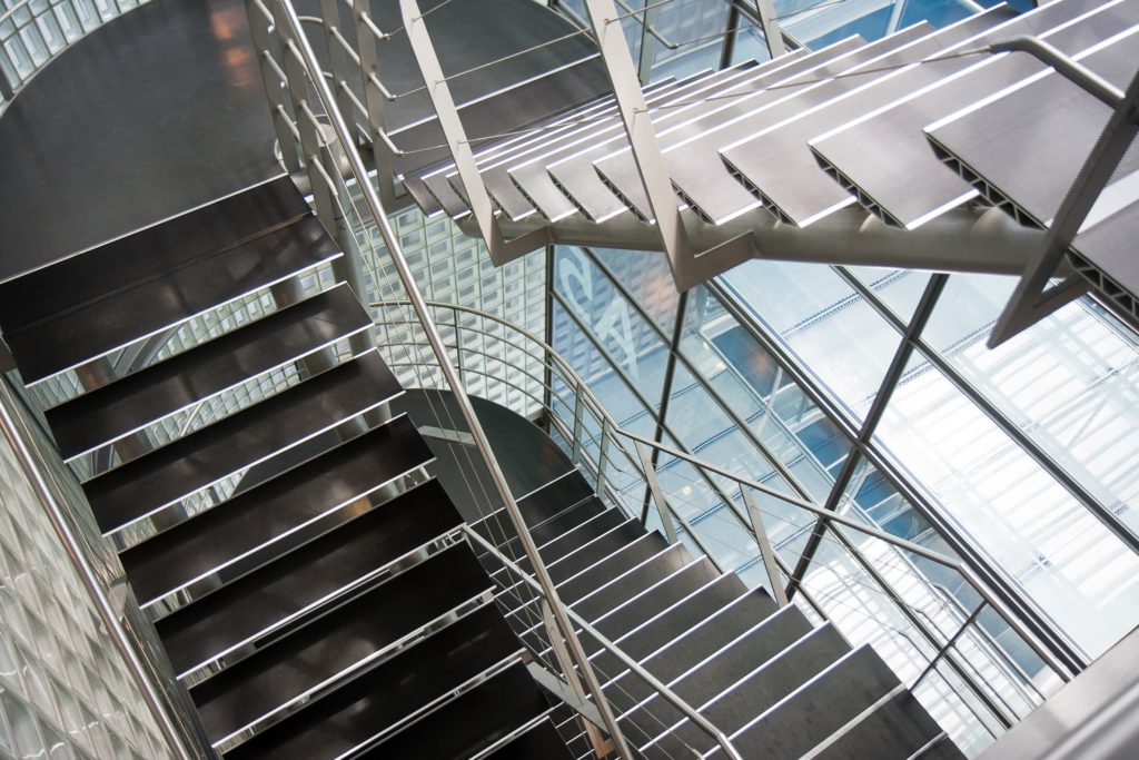 A picture of a set of newly installed steel stairs with tiered railings flanked by windows that overlook the city below. 